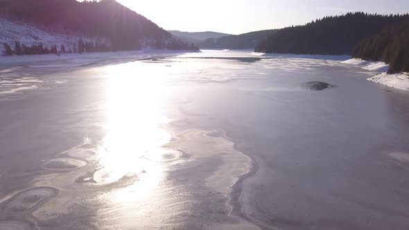 Bright Sunlight Reflection On Frozen Lake Neath The Mountains In Transylvania - Wide Shot