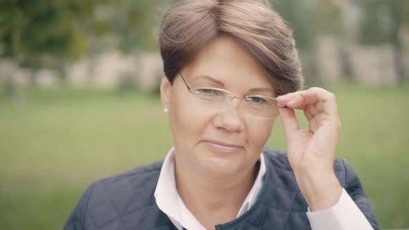 Headshot of Confident Senior Beautiful Woman Putting on Eyeglasses and Smiling at Camera