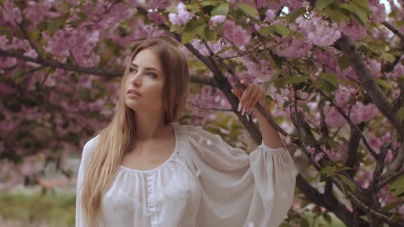 Spring Beauty Portrait of a Woman at Blossoming Sakura Tree on Nature