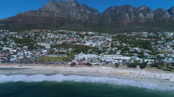 Backwards drone shot over ocean revealing beautiful beach and mountain