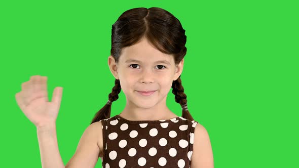 Beautiful Brunette Little Girl in Polka Dot Dress Waving To the Camera on a Green Screen Chroma Key