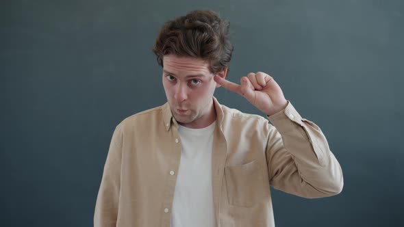 Emotional Young Man Showing Are you Crazy Hand Gesture Twisting Finger Near Head and Looking at