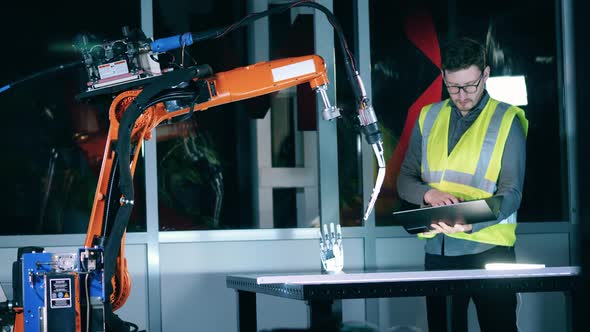 Male Scientist in a Safety Vest Is Watching a Robotic Arm