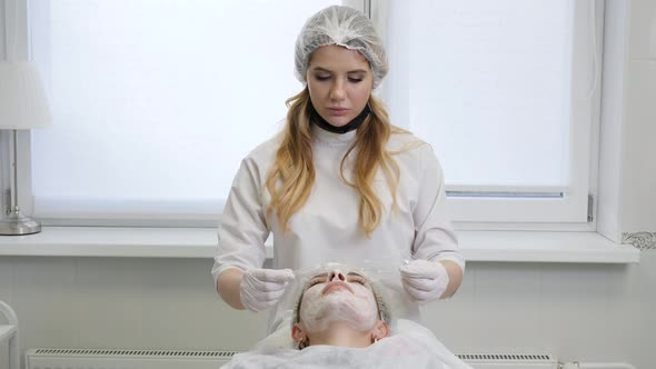 Girl Beautician Wears a Transparent Film on the Patient Lying