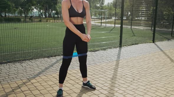 Woman Exercising Squats with Elastic Band Outdoors in Summer