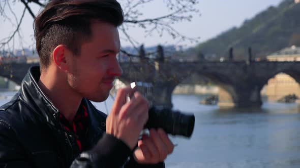 A Young Handsome Man Takes Photos with a Camera - Closeup - a River and a Bridge