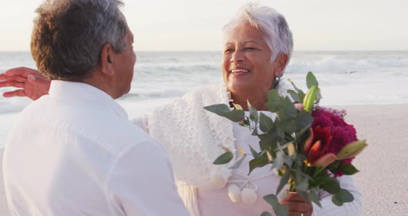 Happy hispanic couple embracing and laughing on beach after proposal