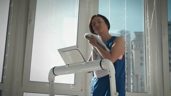 Woman is wiping face with towel during fitness cardio exercises at home in the morning