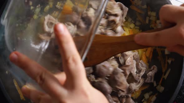 Top view of a woman's hand in a wok with fried onions and carrots poured Chicken Gizzard