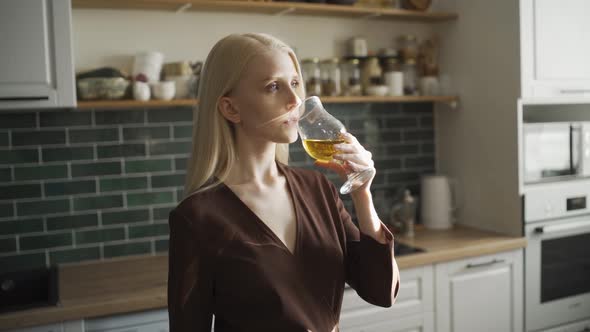 Beautiful Young Blonde Woman Drinks Juice From a Beautiful Glass in the Kitchen