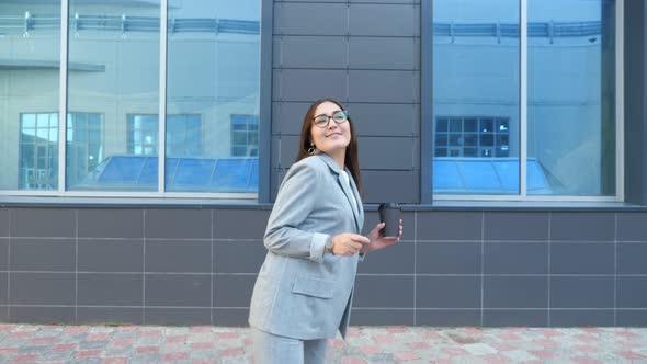 Woman in Glasses and a Suit with a Cup of Coffee Dancing on the Street