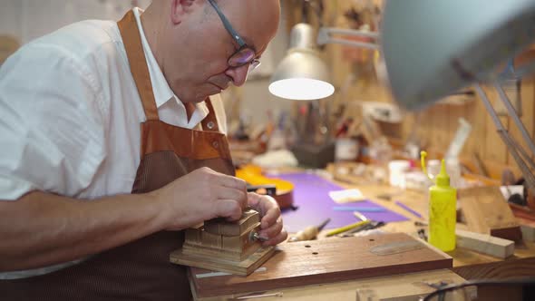 Luthier with violin bridge in workshop