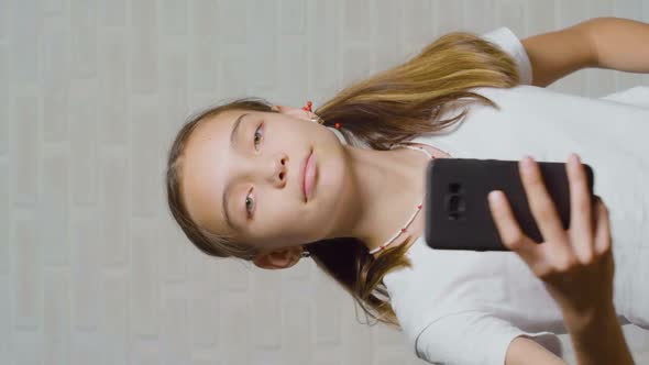 Overconfident Asian Teenage Girl Smiles and Takes Pictures of you with Her Smartphone