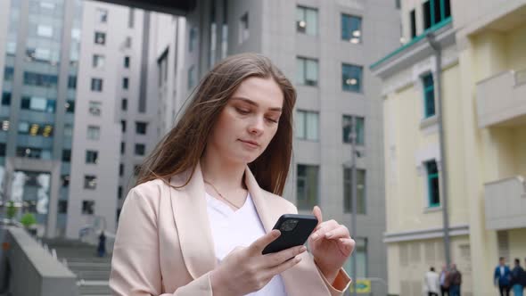 Portrait of Confident Business Woman Typing By Mobile Phone While Walking Outdoors at City Street