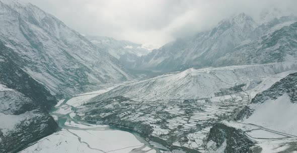 Aerial Cinematic View Of Snow Covered Hussaini Village In Hunza Valley Beside Frozen River. Dolly Ba