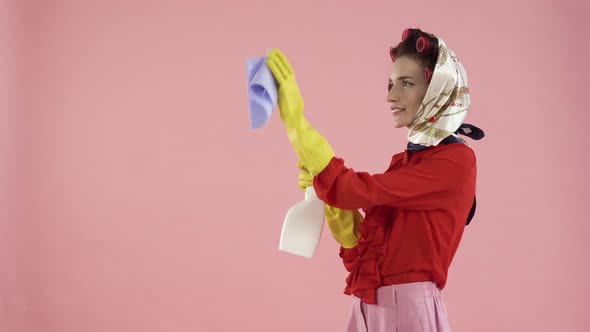 A Woman with a Kerchief on Her Head and Curlers Washes an Invisible Window