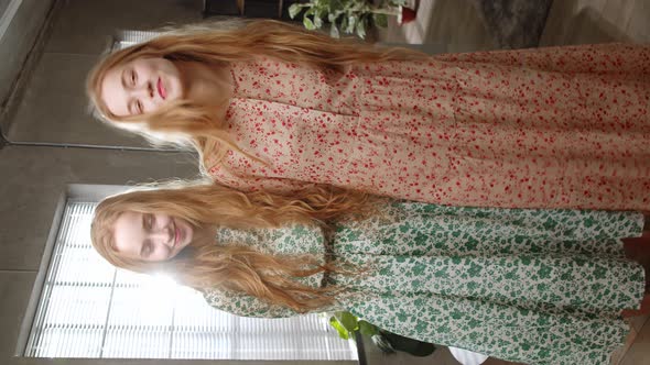 Two Young Sisters Twin Posing and Look Into the Camera in Beautiful Dresses at Home in the Living