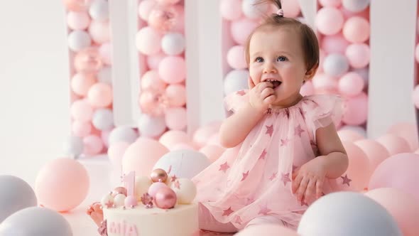 A Cute Little Girl in a Dress Sits Near a Birthday Cake with the Number 1