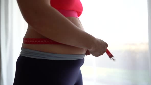 Young Woman Measures Her Waist with a Tape Measure Closeup