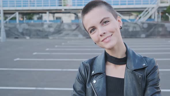 Portrait of Smiling Young Woman with Short Hair in Industrial City Background at Sunset