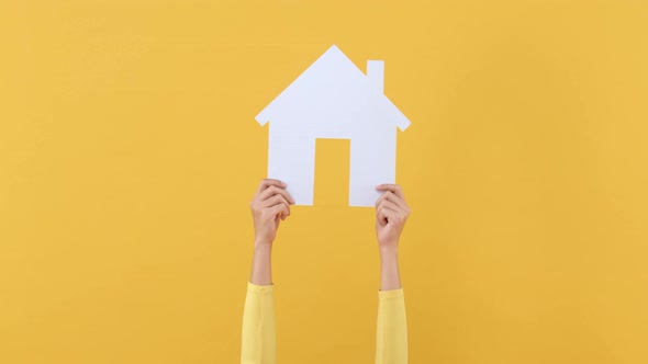 Hands holding home cutout model and shaking left and right on isolated yellow background