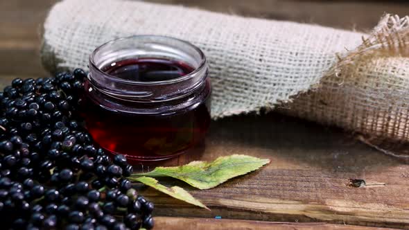 In Slow Motion Camera Natural Elderberry Juice In A Glass Jar On Wooden Boards.