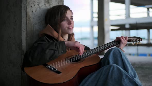 Side View of Beautiful Young Lonely Woman Playing Guitar in Abandoned Building