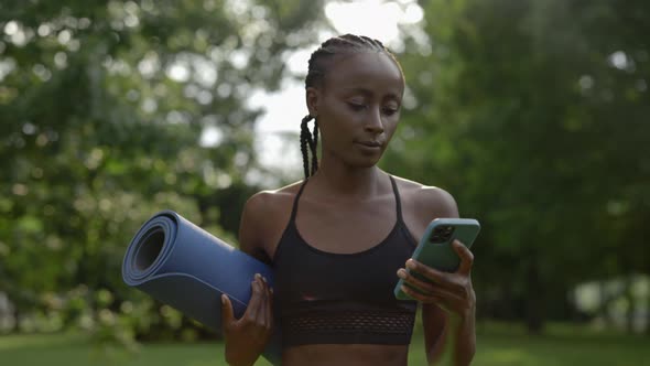 African American Woman Using Mobile and Carrying Yoga Mat