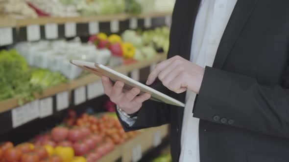 Close-up of Male Caucasian Hands Using Tablet in Grocery Store. Unrecognizable Adult Man in Suit