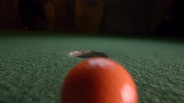 An orange mini golf ball slowly falls into the golf hole and bounces in the pocket on a course.