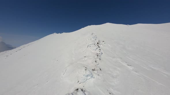 Climbing Near Soft Smooth Snow Cover Surface on High Mountain Ridge Peak Under Blue Sky Aerial View