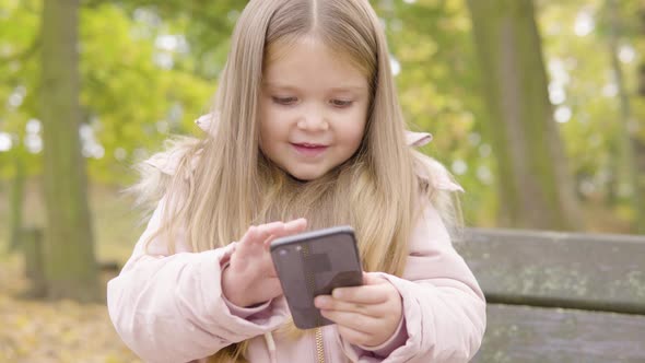 Cute Little Caucasian Girl Plays with a Smartphone and Smiles Then Gets Help From Her Mom