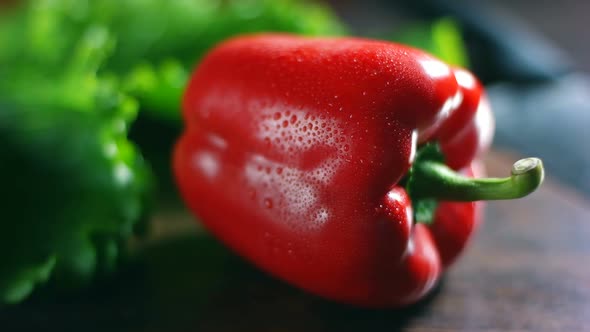 Red bell pepper paprika with water drops on a wooden board, green salad leaves on background, dolly