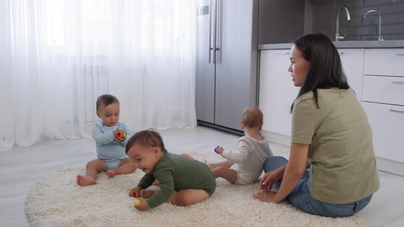 Happy Asian Woman Relaxing on Carpet with Baby Triplets alt