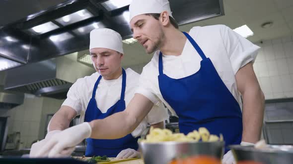 Portrait of Confident Professional Young Chef Talking to Unsure Cook Pointing at Order Recipe