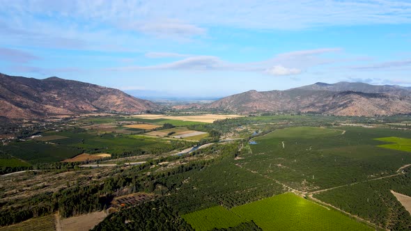 Aerial panning of green farm field surrounded by mountains on a cloudy day, Cachapoal Valley, south