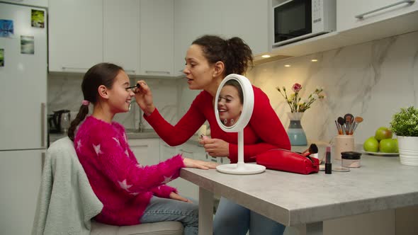 Positive Mother Teaching Cute Young Girl Making Makeup at Home