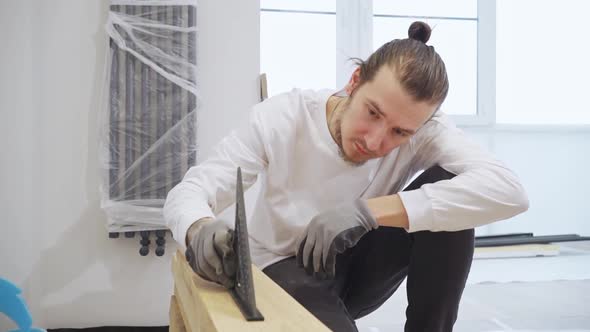 Carpenter in Protective Gloves Makes Measurements Using a Triangle on Wood