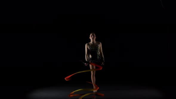 Gymnast Gracefully Move with a Ribbon in His Hands. Black Background