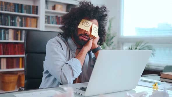 Young African American Man Freelancer Sits and Sleeping with Stickers Closed Eyes