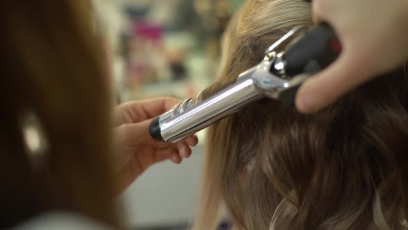 Closeup of Professional Female Hairdresser Making Hairstyle Using Curling Iron