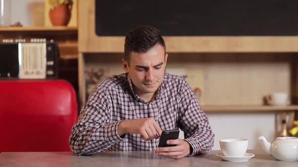 Happy Attractive Man in Shirt Using App on Smartphone in the Kitchen.