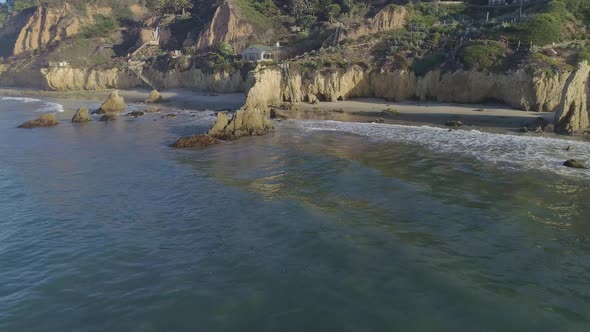 Aerial shots of El Matador beach over breaking waves and rocks on a hazy summer morning in Malibu, C