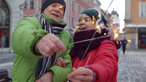 Senior Couple Holding Sparklers Bengal Lights Enjoying Christmas Eve Making Kiss in Winter City