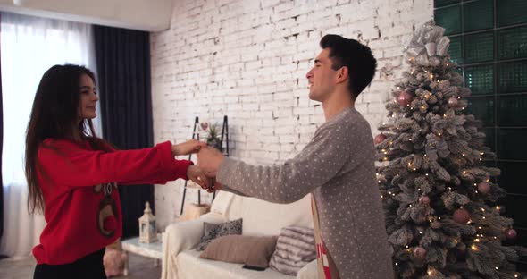 The Guy Dances with the Girl in Winter Sweaters on a Background of the Christmas Room