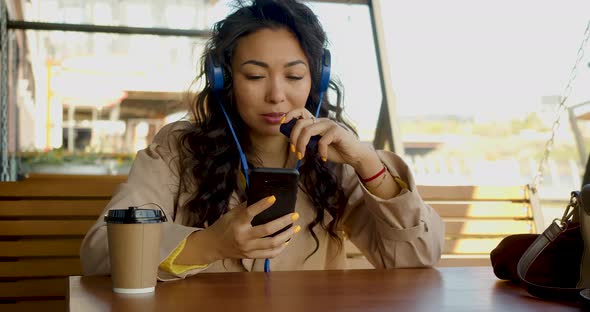 An Asian Woman Sits in Headphones Messaging on Social Networks Through an Online Smartphone App and