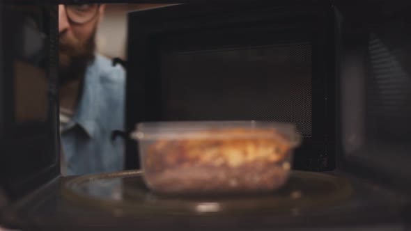 Man Putting Leftover Dinner Into Microwave Oven To Cook