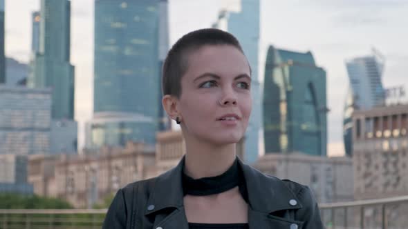 Young Woman with Shaved Hair Walking Against Urban Background with Skyscrapers. 