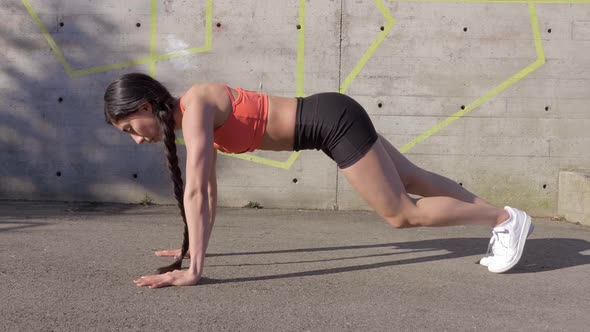 Fit athletic woman doing plank knee raises outdoors