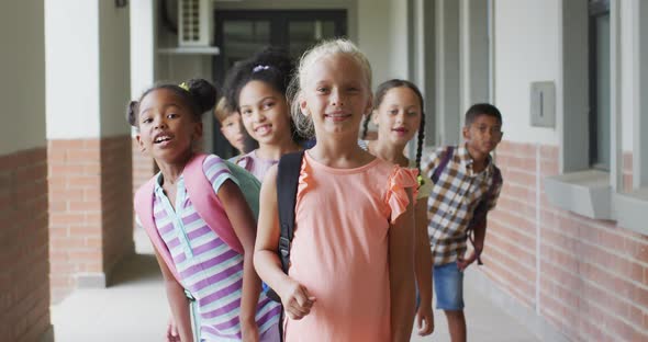 Video of happy caucasian girl and diverse pupils at schoot corridor